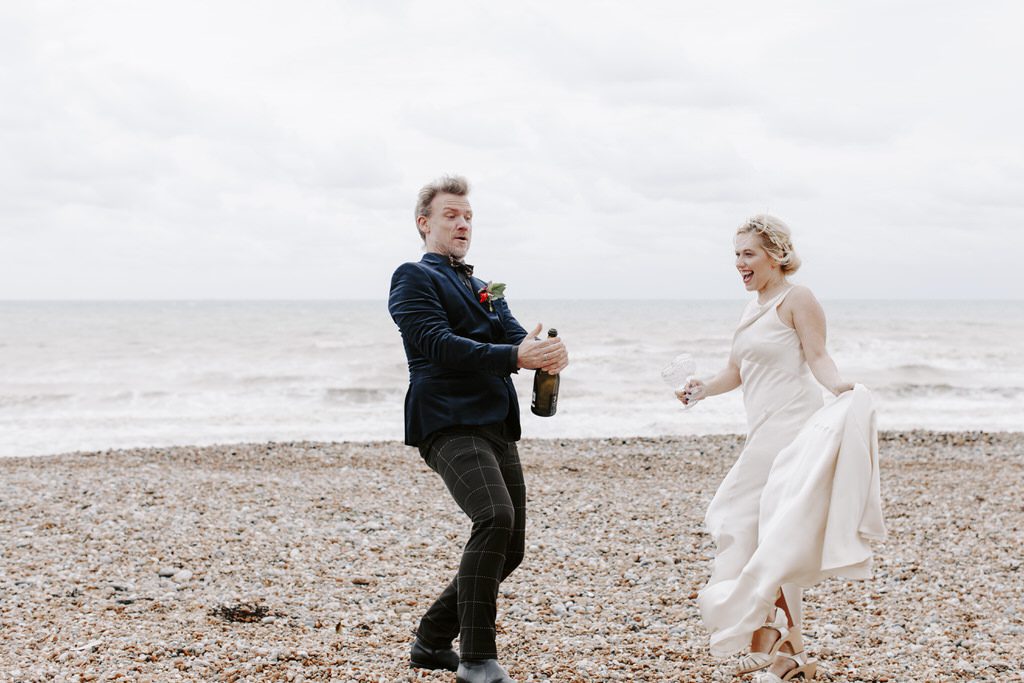 Newlyweds opening a champagne on a beach in Hastings